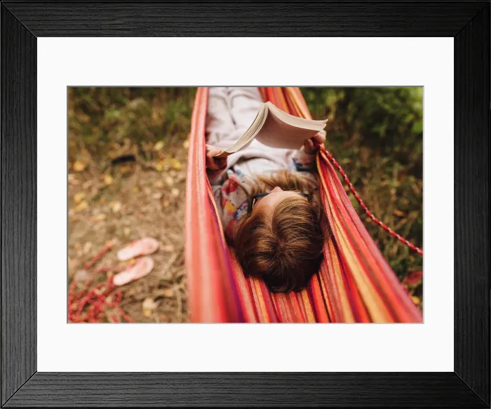 Framed Print : Little girl reads a book in hammock on a warm fall day while camping Framed Print : Little girl reads a book in hammock on a warm fall day while camping