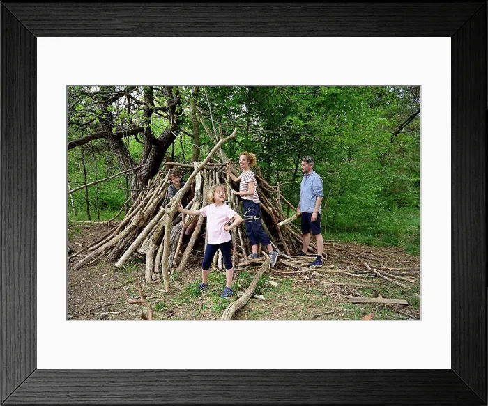 Framed Print : Girl holding log while building camp with family in forest