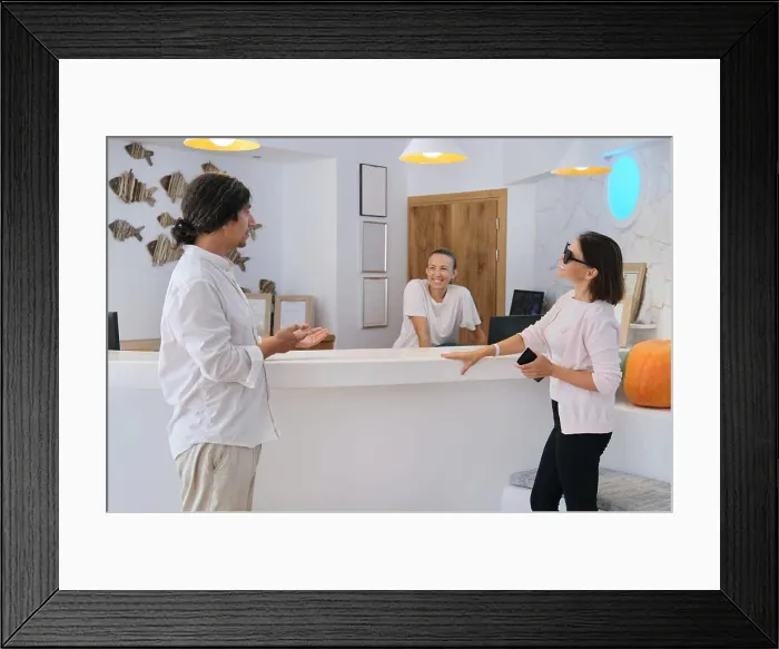 Framed Print : Smiling woman guest near reception desk, friendly man and woman hotel workers