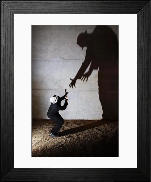 Framed Print : Man cowering from tall ominous shadow on wall Framed Print : Man cowering from tall ominous shadow on wall