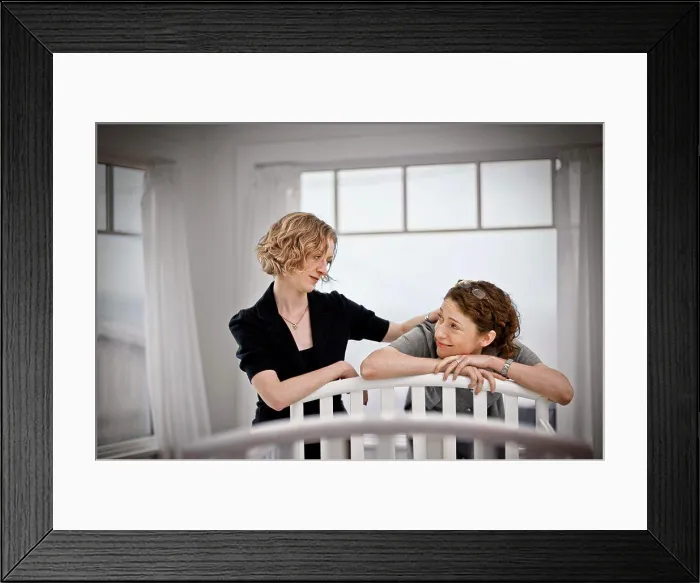 Framed Print : Lesbian couple looking reassuredly at each other while standing beside a cot in a nursery Framed Print : Lesbian couple looking reassuredly at each other while standing beside a cot in a nursery