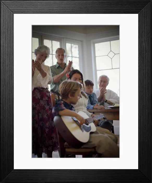 Framed Print : Happy family listening to a young boy playing a guitar at the dinner table Framed Print : Happy family listening to a young boy playing a guitar at the dinner table