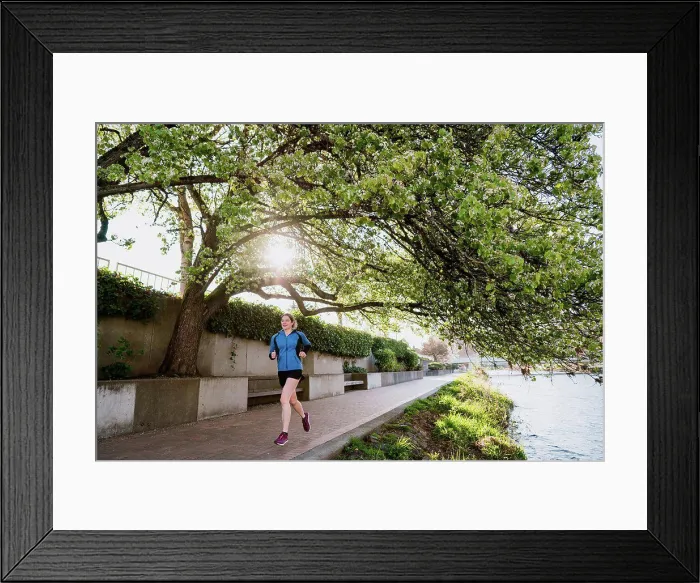 Framed Print : Young woman runs on paved path through a tree tunnel next to river Framed Print : Young woman runs on paved path through a tree tunnel next to river