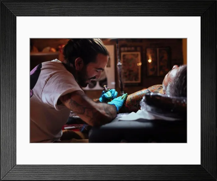 Framed Print : Tattoo artist enjoys while working on a customer's arm in his studio Framed Print : Tattoo artist enjoys while working on a customer's arm in his studio