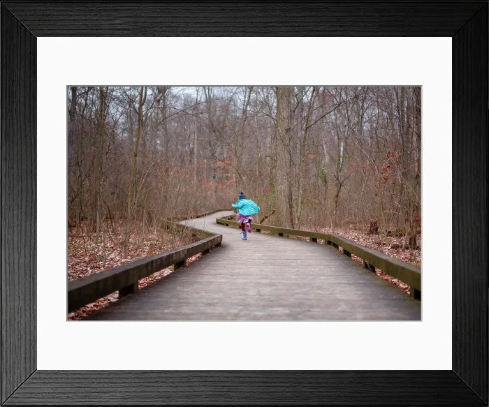 Framed Print : Girl in bright blue coat runs down wooded path in woods in autumn Framed Print : Girl in bright blue coat runs down wooded path in woods in autumn