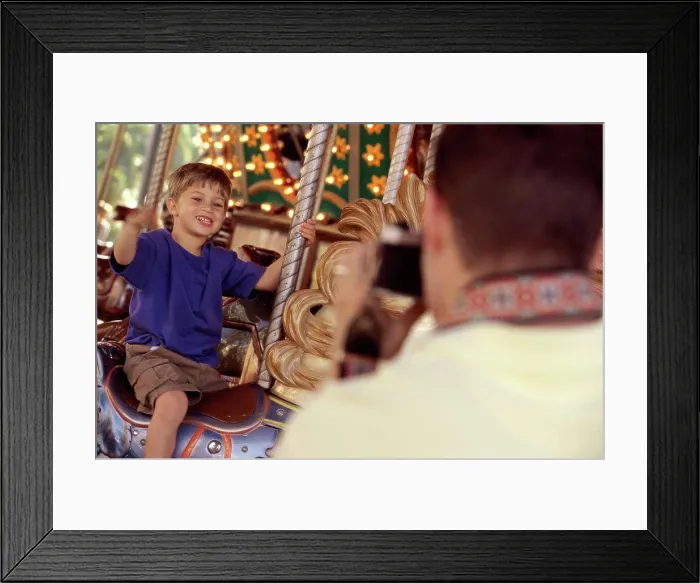 Framed Print : Rear view of a father taking a photograph of his son riding a carousel horse