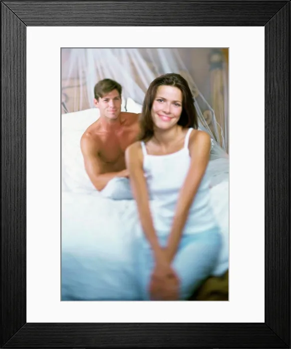 Framed Print : Portrait of a young woman smiling with a young man sitting behind her on a bed Framed Print : Portrait of a young woman smiling with a young man sitting behind her on a bed