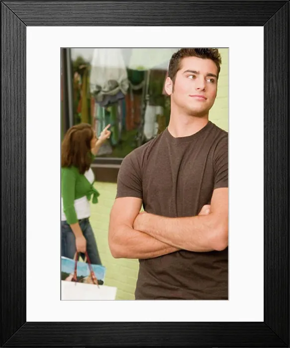 Framed Print : Close-up of a teenage boy looking sideways with a young woman shopping behind him
