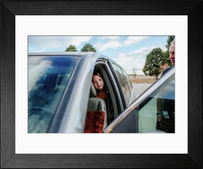 Framed Print : Young girl peeking out from back seat of a car before a trip