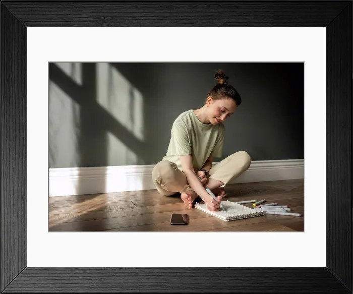 Framed Print : Smiling woman drawing on note pad while sitting on floor Framed Print : Smiling woman drawing on note pad while sitting on floor