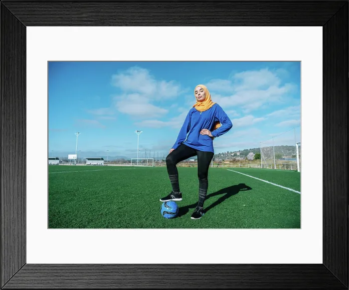Framed Print : Arab female football player with ball on field