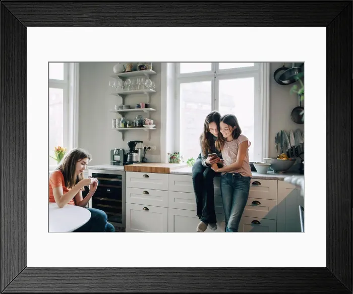 Framed Print : Female friends using mobile phone in kitchen at home Framed Print : Female friends using mobile phone in kitchen at home