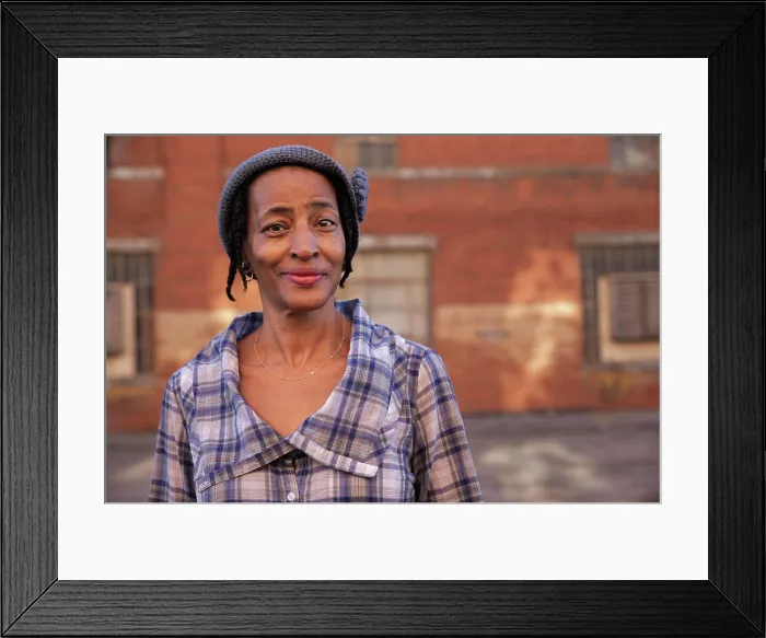 Framed Print : Portrait of older woman wearing knit hat standing in alley smiling looking at camera, brick wall in background Framed Print : Portrait of older woman wearing knit hat standing in alley smiling looking at camera, brick wall in background