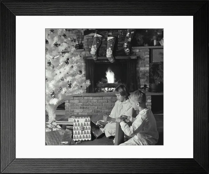 Framed Print : Side profile of a girl and her brother unwrapping Christmas presents near a fireplace Framed Print : Side profile of a girl and her brother unwrapping Christmas presents near a fireplace