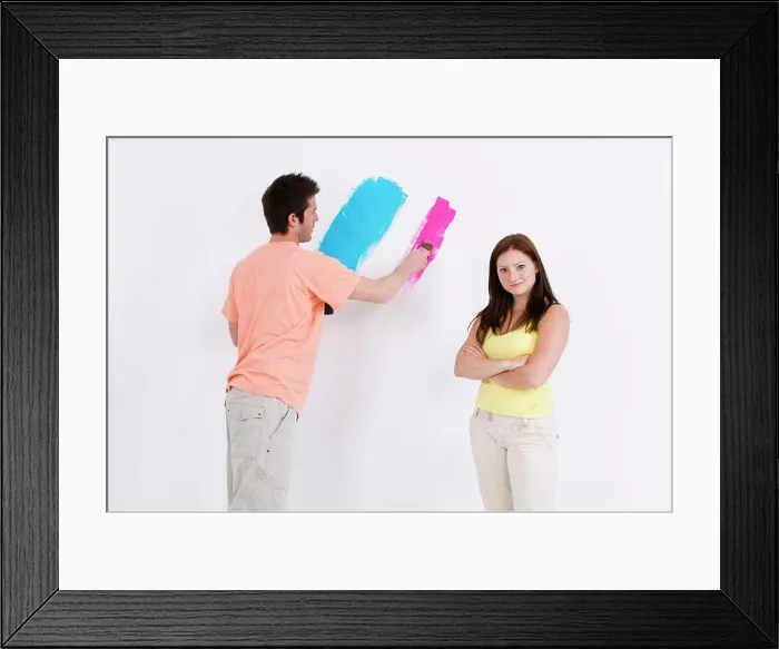 Framed Print : Young man painting a wall with a young woman standing beside him Framed Print : Young man painting a wall with a young woman standing beside him