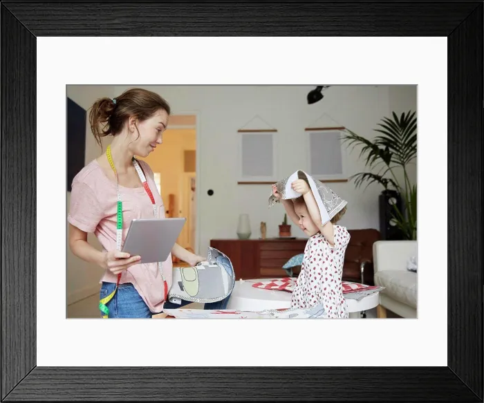 Framed Print : Fashion designer with digital tablet looking at playful daughter holding textile Framed Print : Fashion designer with digital tablet looking at playful daughter holding textile