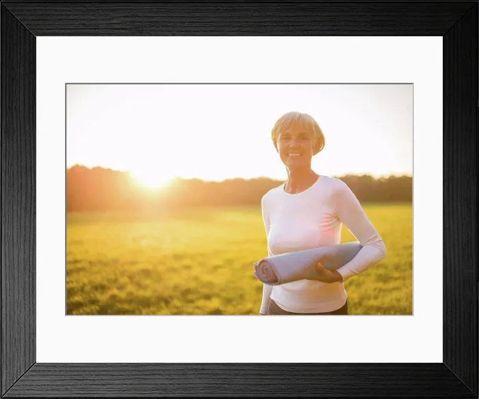 Framed Print : Portrait of smiling senior woman holding yoga mat on rural meadow at sunset