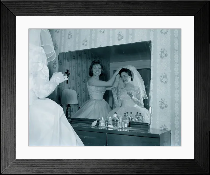 Framed Print : Bridesmaid attaching veil to bride's hair in front of mirror
