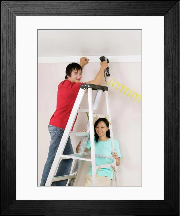 Framed Print : Portrait of a young man using a drill on a wall with a young woman holding a ladder Framed Print : Portrait of a young man using a drill on a wall with a young woman holding a ladder