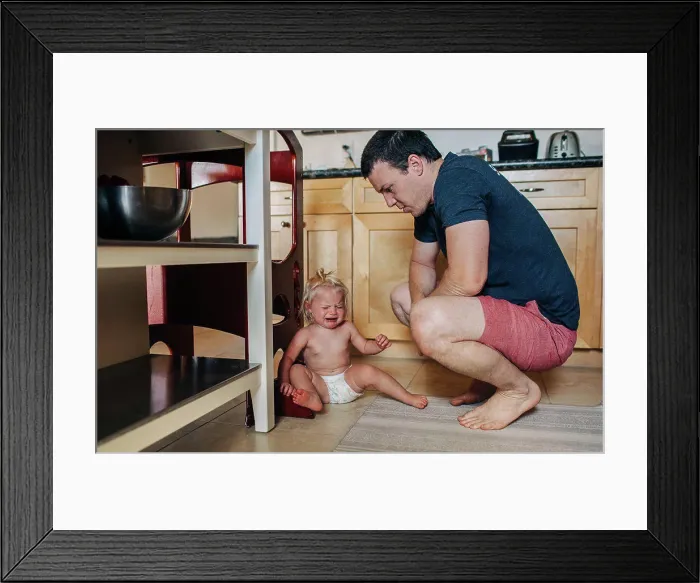 Framed Print : Dad looks down at diapered toddler girl while crying in kitchen Framed Print : Dad looks down at diapered toddler girl while crying in kitchen