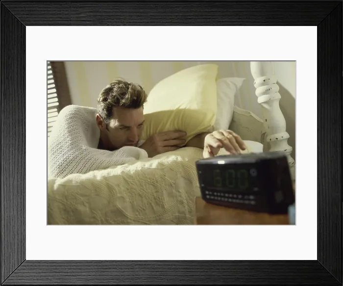 Framed Print : Young man lying on a bed reaching for the alarm clock