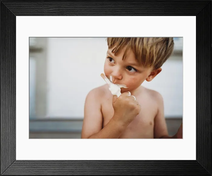 Framed Print : Cute young boy eating ice cream looking to the side outside in summer Framed Print : Cute young boy eating ice cream looking to the side outside in summer