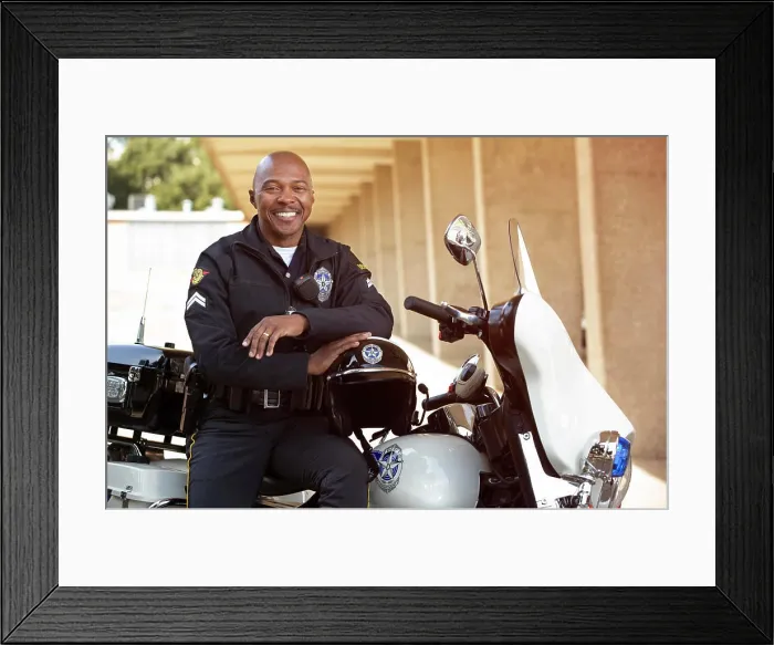 Framed Print : Portrait of Police officer sitting on his motorcycle outside looking towards camera smiling