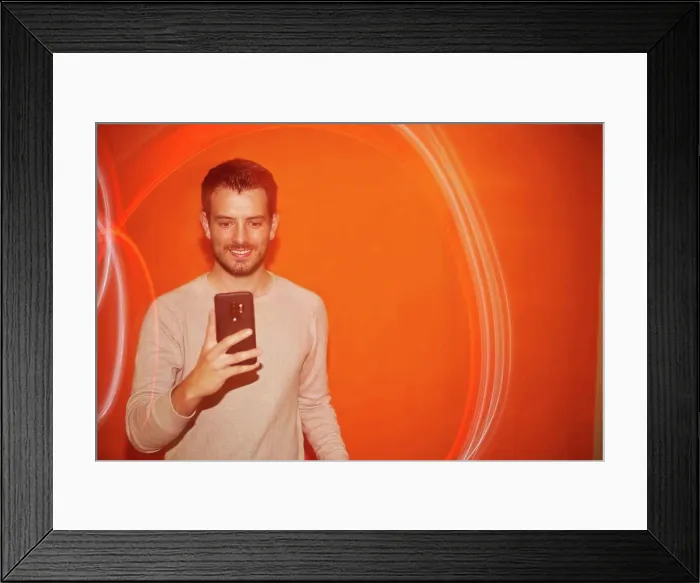 Framed Print : Young man looking the smartphone on a orange colored background