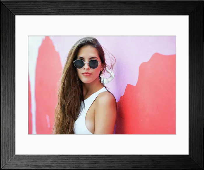 Framed Print : Young woman with long hair wearing stylish sunglasses and standing near red building wall in city