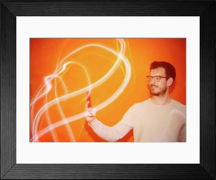 Framed Print : Young man looking the smartphone on a orange colored background Framed Print : Young man looking the smartphone on a orange colored background