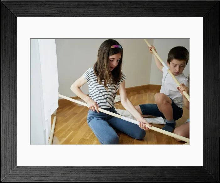 Framed Print : Girl putting the sticks to build a teepee tent inside their house. Creativity concept Framed Print : Girl putting the sticks to build a teepee tent inside their house. Creativity concept