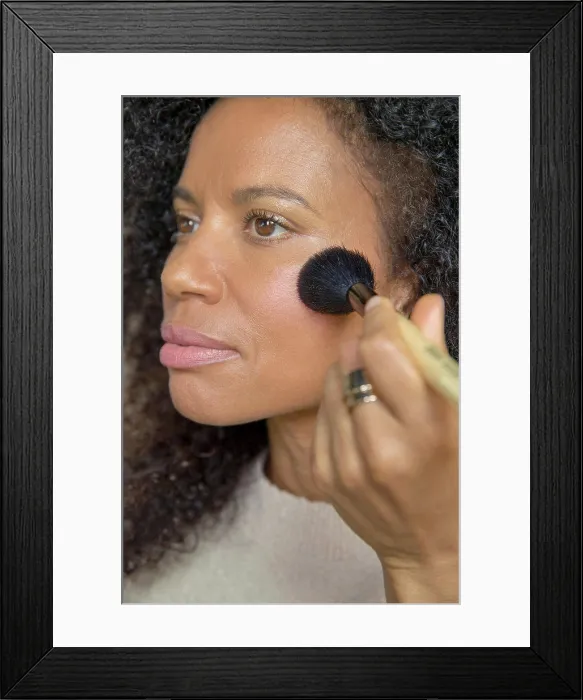 Framed Print : Mixed race, middle-aged woman looks off camera while putting on make up Framed Print : Mixed race, middle-aged woman looks off camera while putting on make up