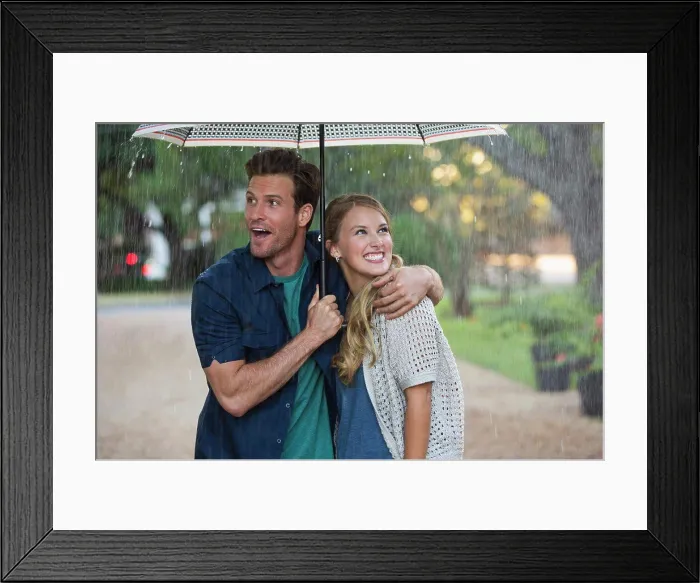 Framed Print : Young couple walking through park with umbrella in the rain, both looking out at the falling rain