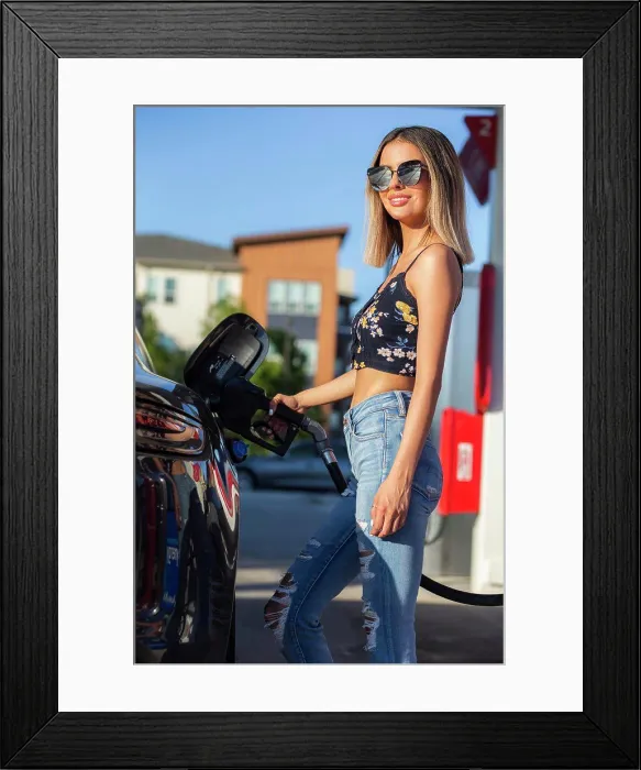Framed Print : Confident girls stating outside at gas station pumping gas into car, wearing sunglasses Framed Print : Confident girls stating outside at gas station pumping gas into car, wearing sunglasses