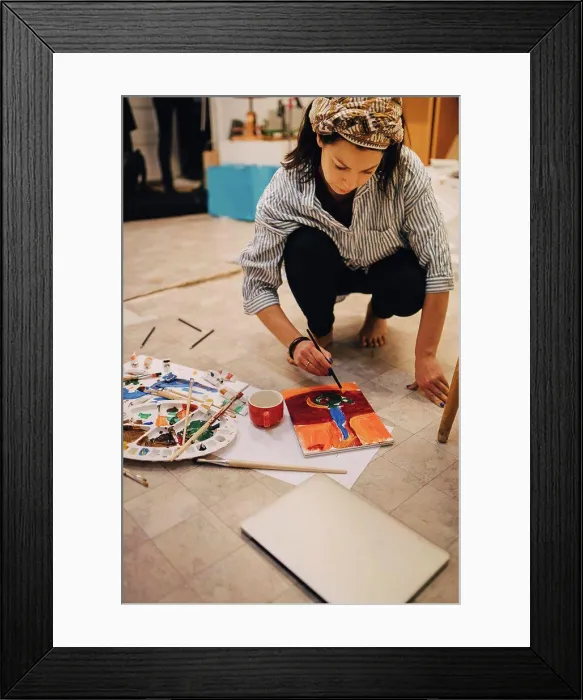 Framed Print : Female artist painting on paper while crouching at art studio Framed Print : Female artist painting on paper while crouching at art studio