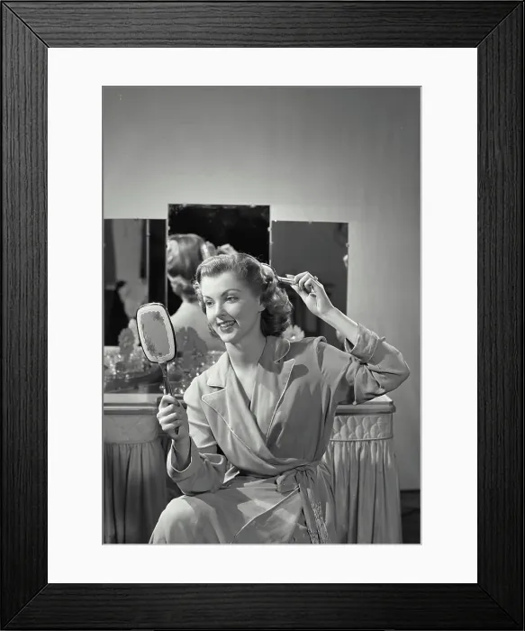 Framed Print : Vintage Photograph. Woman wearing robe combing hair holding up mirror with vanity table in background