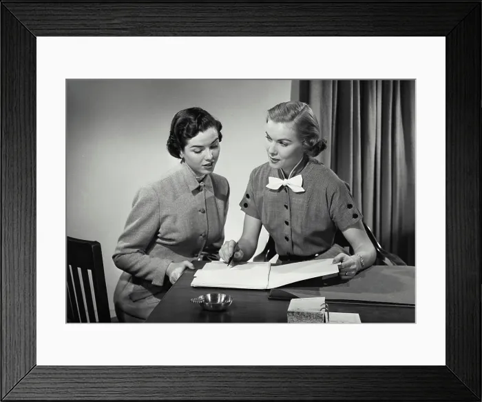 Framed Print : Vintage Photograph. Two women in business office sitting at desk having conversation Framed Print : Vintage Photograph. Two women in business office sitting at desk having conversation