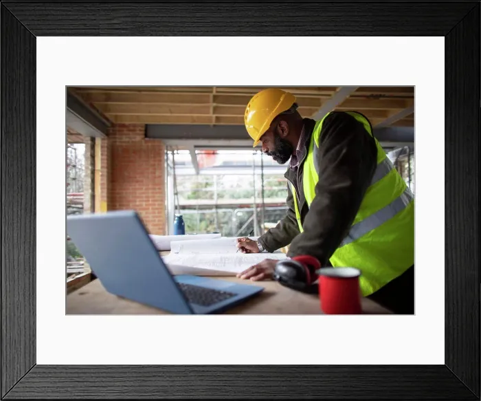 Framed Print : Male architect reviewing blueprints at construction site