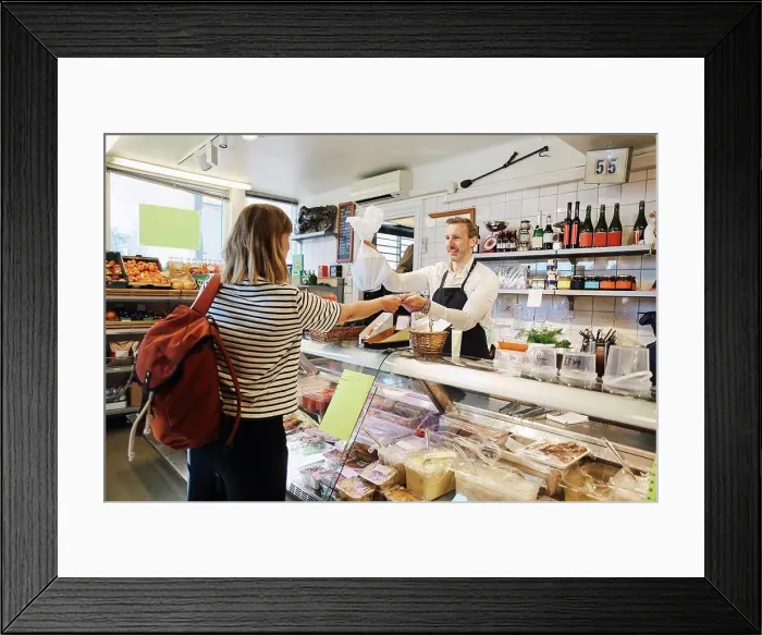 Framed Print : Male sales clerk holding plastic bag while accepting credit card from customer at checkout counter Framed Print : Male sales clerk holding plastic bag while accepting credit card from customer at checkout counter