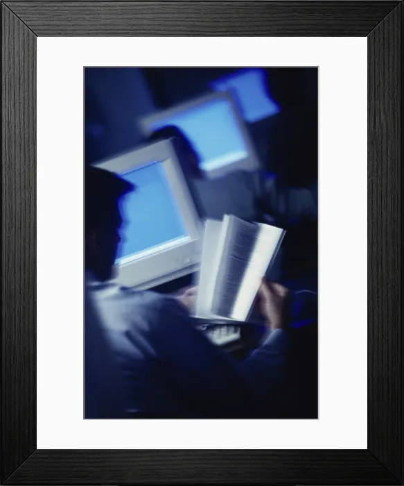 Framed Print : Rear view of a man reading a book in front of a computer monitor