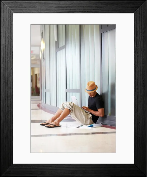 Framed Print : Side profile of a college student sitting in a corridor and using a laptop Framed Print : Side profile of a college student sitting in a corridor and using a laptop