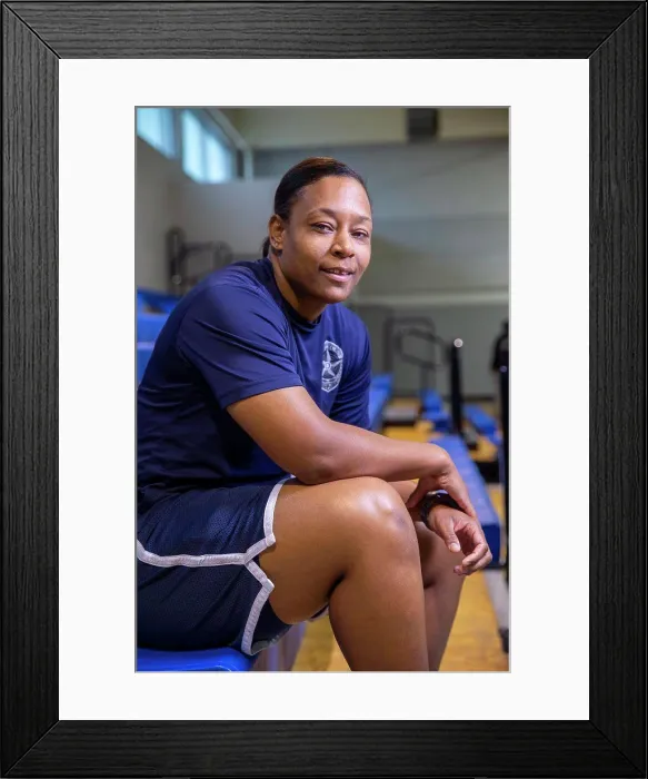 Framed Print : Portrait of Police woman sitting on bleachers in gymnasium looking towards camera smiling