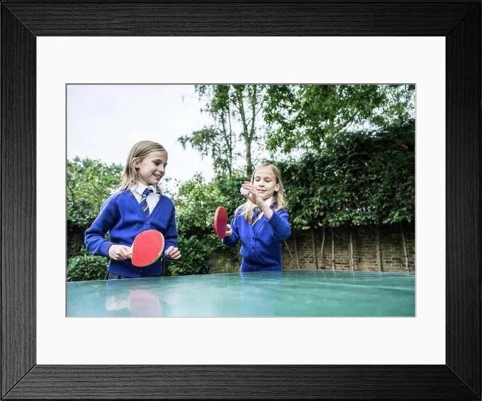 Framed Print : Twin girls in school uniform playing table tennis outside Framed Print : Twin girls in school uniform playing table tennis outside