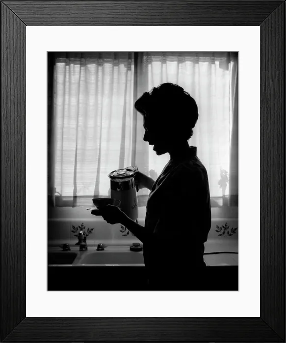 Framed Print : 1970s SILHOUETTED ANONYMOUS WOMAN HOUSEWIFE SPEAKING WHILE POURING FIRST CUP OF MORNING COFFEE IN KITCHEN