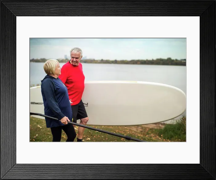 Framed Print : Senior couple carrying paddle boarding equipment Framed Print : Senior couple carrying paddle boarding equipment