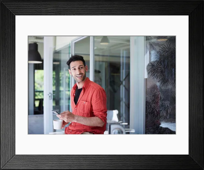 Framed Print : Creative businessman looking away while using mobile phone in office during coffee break