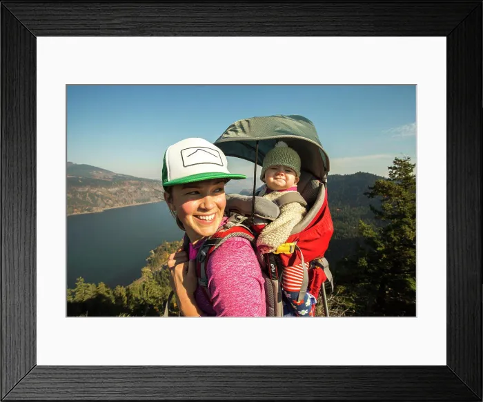 Framed Print : A young woman stands atop a mountain with a baby in a backpack Framed Print : A young woman stands atop a mountain with a baby in a backpack
