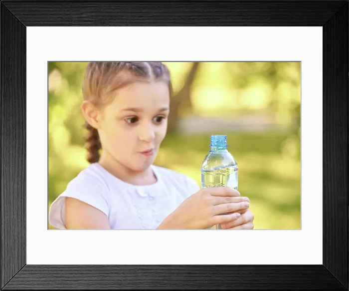 Framed Print : Überrascht kaukasischen weiblichen Kind hält Wasserflasche außerhalb in sonnigen Park Surprised caucasian female child