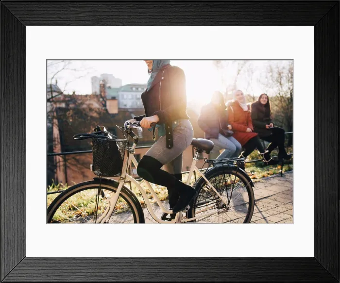 Framed Print : Low section of woman cycling by female friends sitting on railing in city