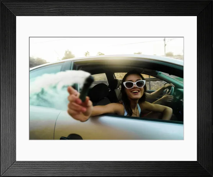 Framed Print : Side view of young cheerful girl in sunglasses riding in car and holding gas bomb Framed Print : Side view of young cheerful girl in sunglasses riding in car and holding gas bomb